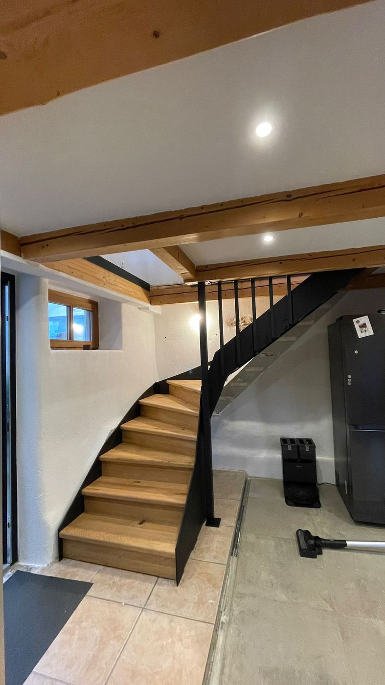 Gewendelte Holztreppe mit schwarzem Stahlgeländer im hellen Innenraum.